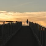 silhouette photography of man standing on corner of bridge